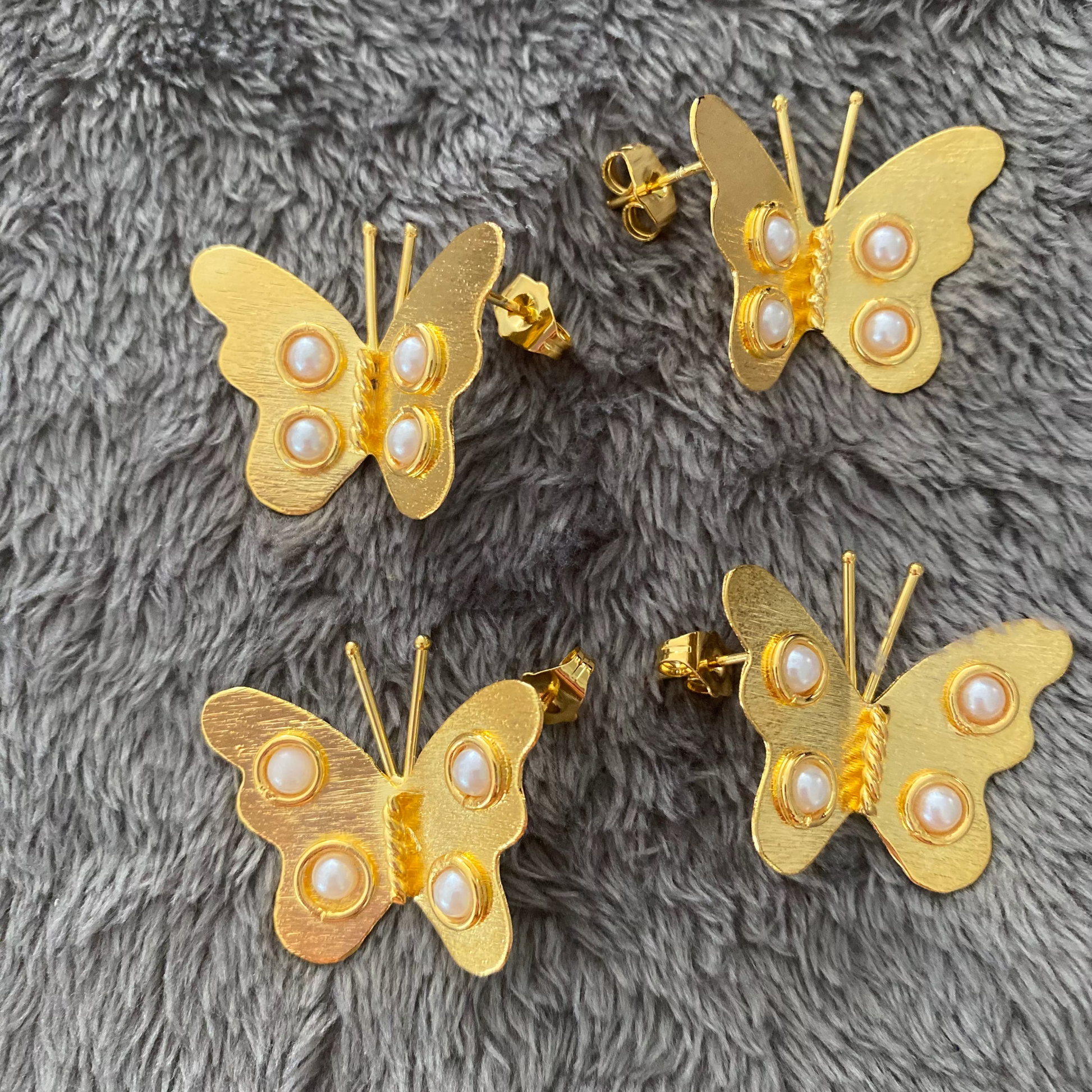 Gold butterfly earrings with pearl centers on a gray textured surface