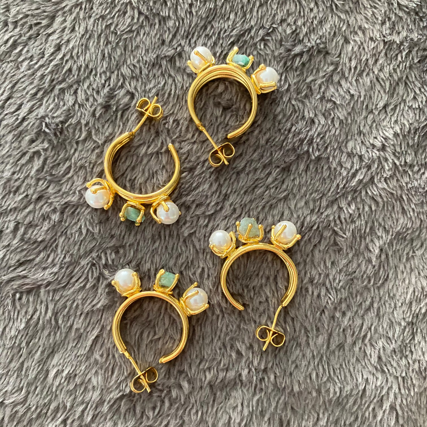 Set of gold hoop earrings with pearl-like stones on a gray textured surface