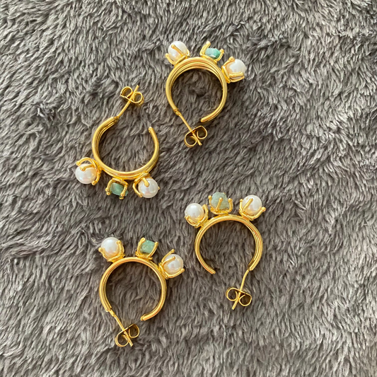 Set of gold hoop earrings with pearl-like stones on a gray textured surface