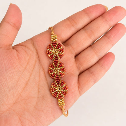 A gold and red beaded bracelet held in a person's hand against a plain light background.