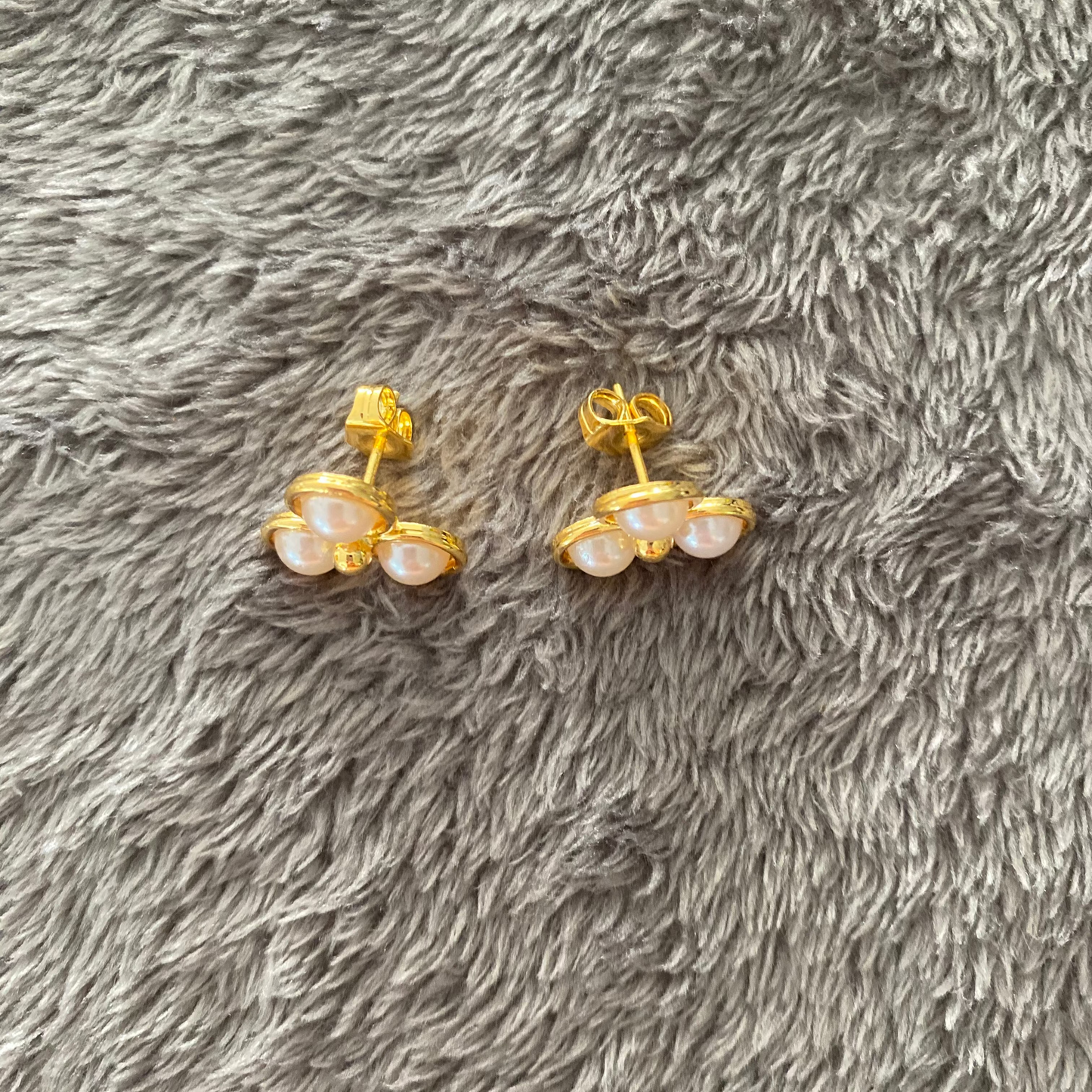 Pair of gold earrings with pearl-like stones on a gray textured surface