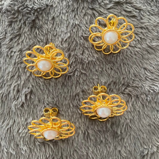 Four gold floral-shaped jewelry components with pearl centers on a gray textured surface