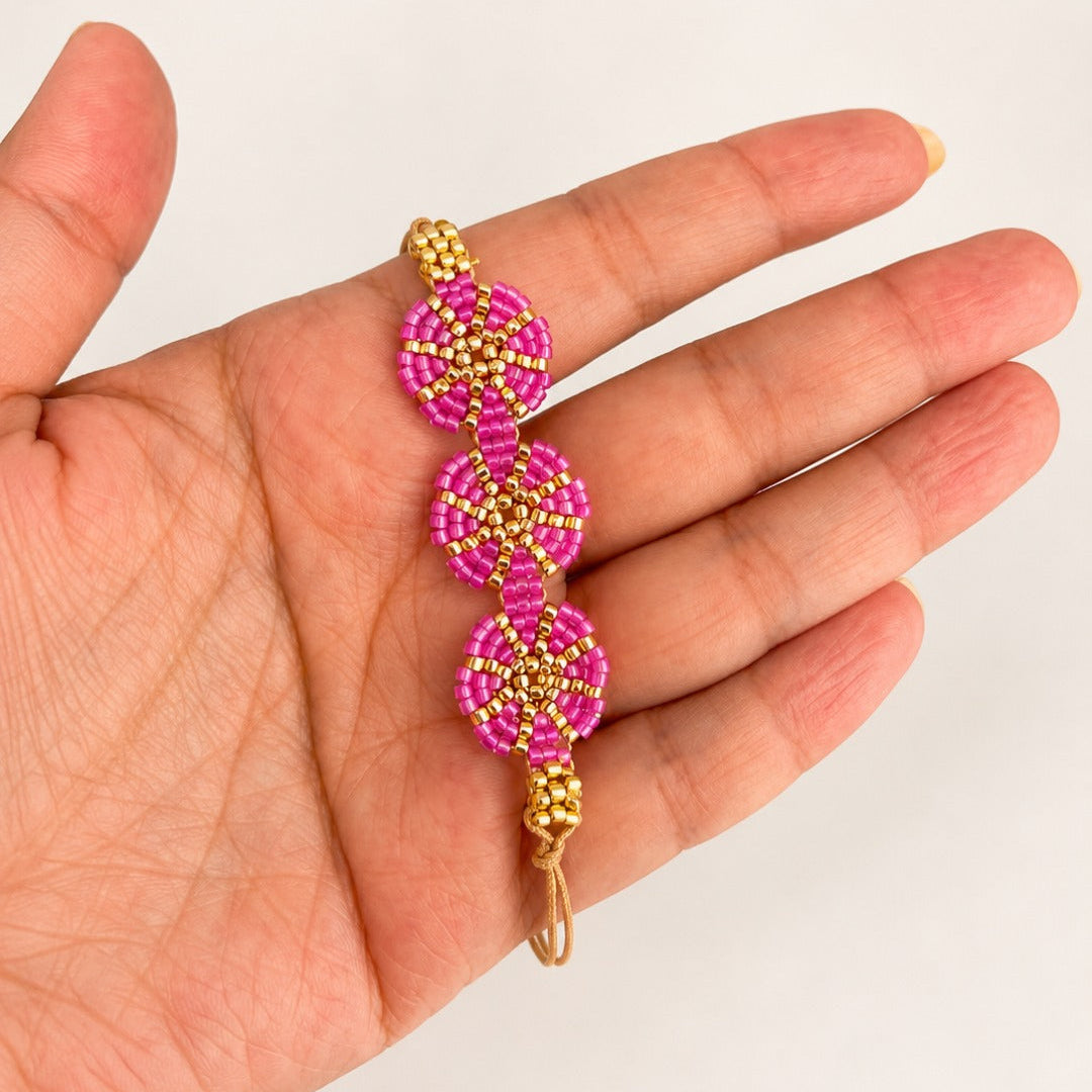 A handmade beaded bracelet with three pink and gold floral clusters held in a person's hand against a plain white background.