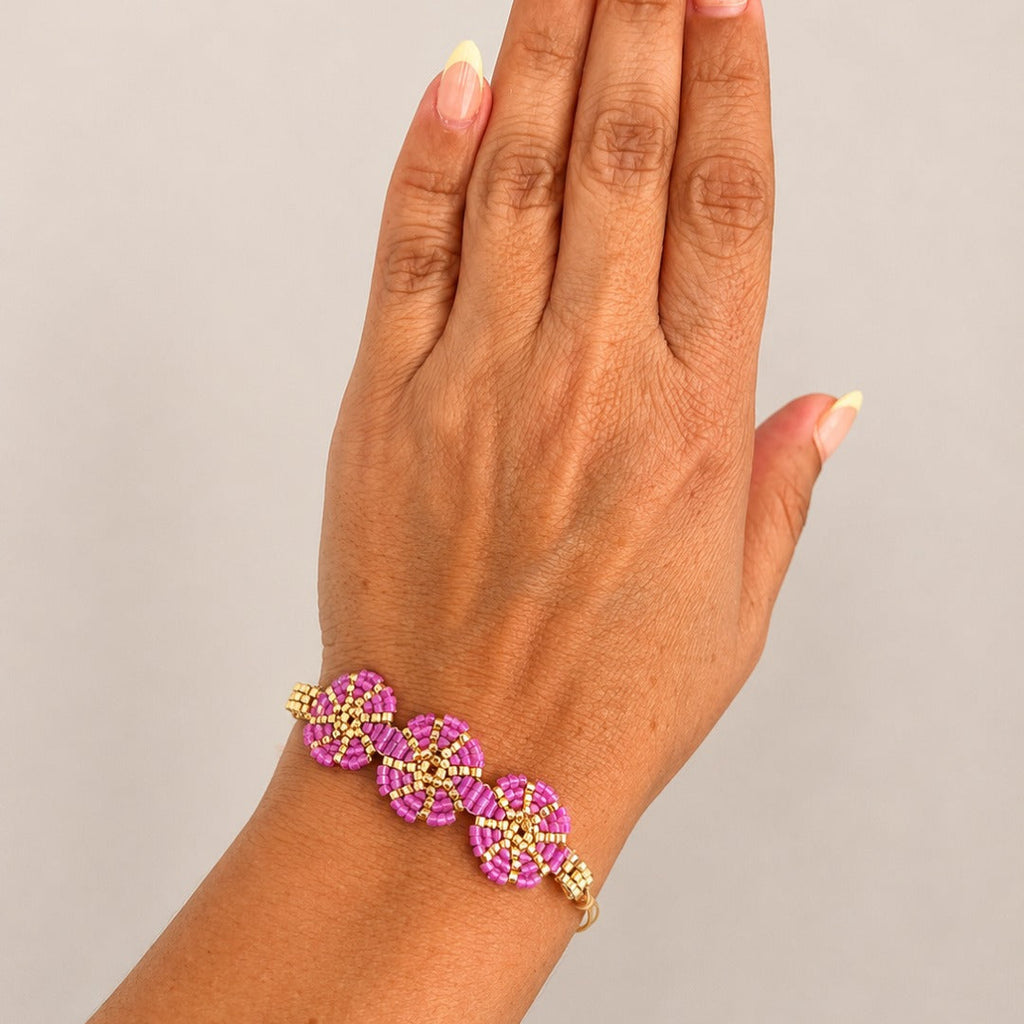 A gold-toned bracelet with three pink floral links, shown worn on a person's wrist against a plain light gray background.