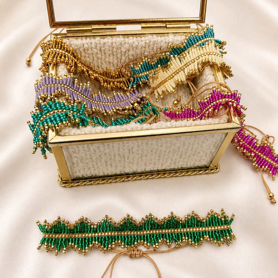 A gold-framed open jewelry box filled with colorful beaded accessories, including a green beaded choker with gold beads and matching cord, displayed on a white satin background.