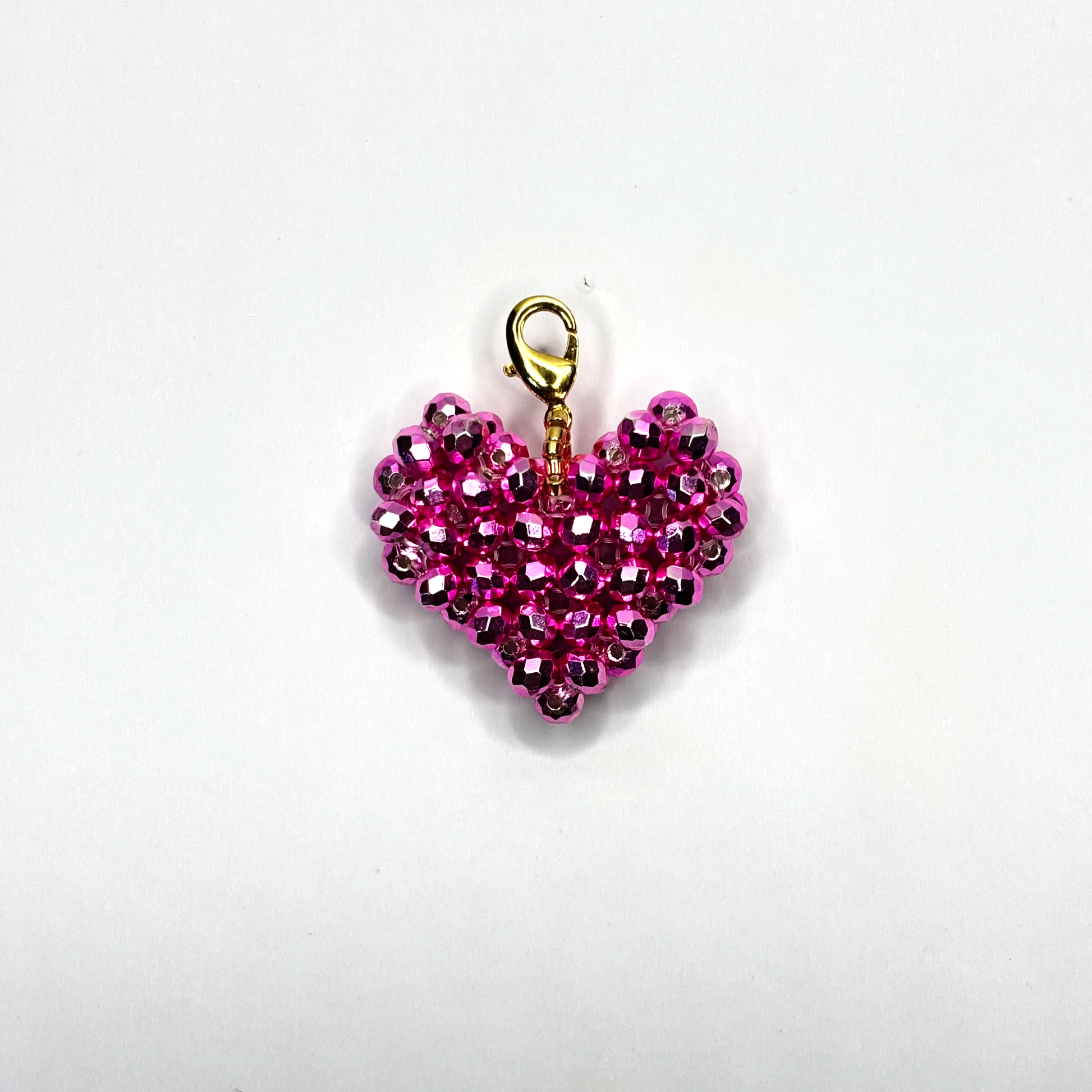 Pink beaded heart charm with gold clasp on a white background
