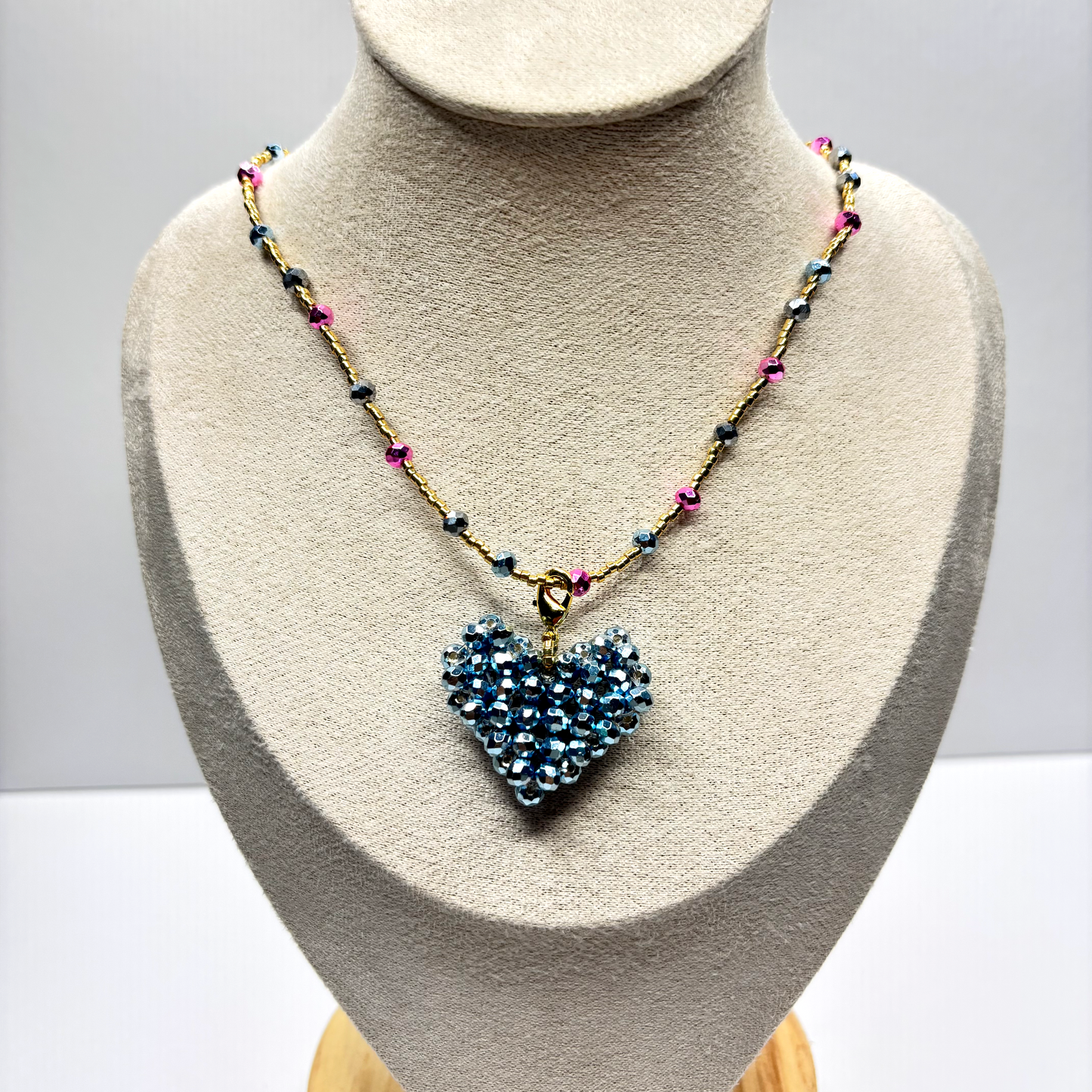 Necklace with a heart-shaped blue pendant on a mannequin bust against a gray background