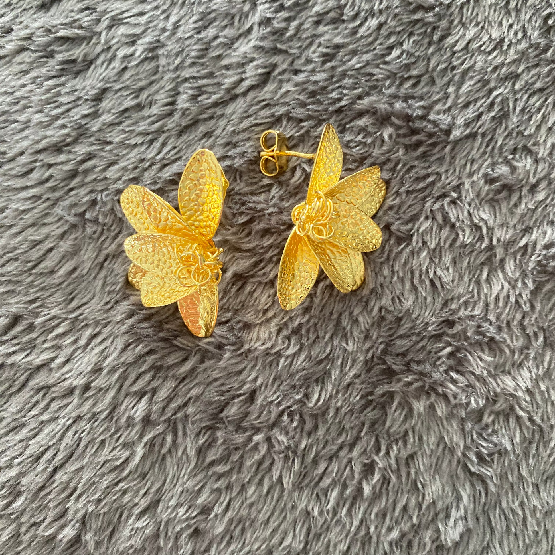 Gold half flower earrings on a gray textured surface