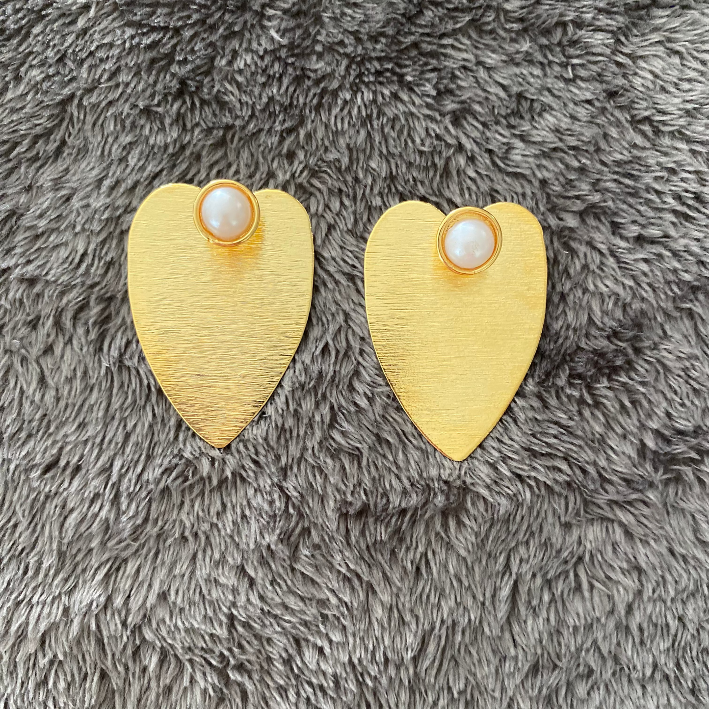 Heart-shaped gold earrings with pearl centers on a gray fluffy surface