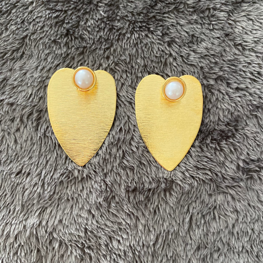 Heart-shaped gold earrings with pearl centers on a gray fluffy surface