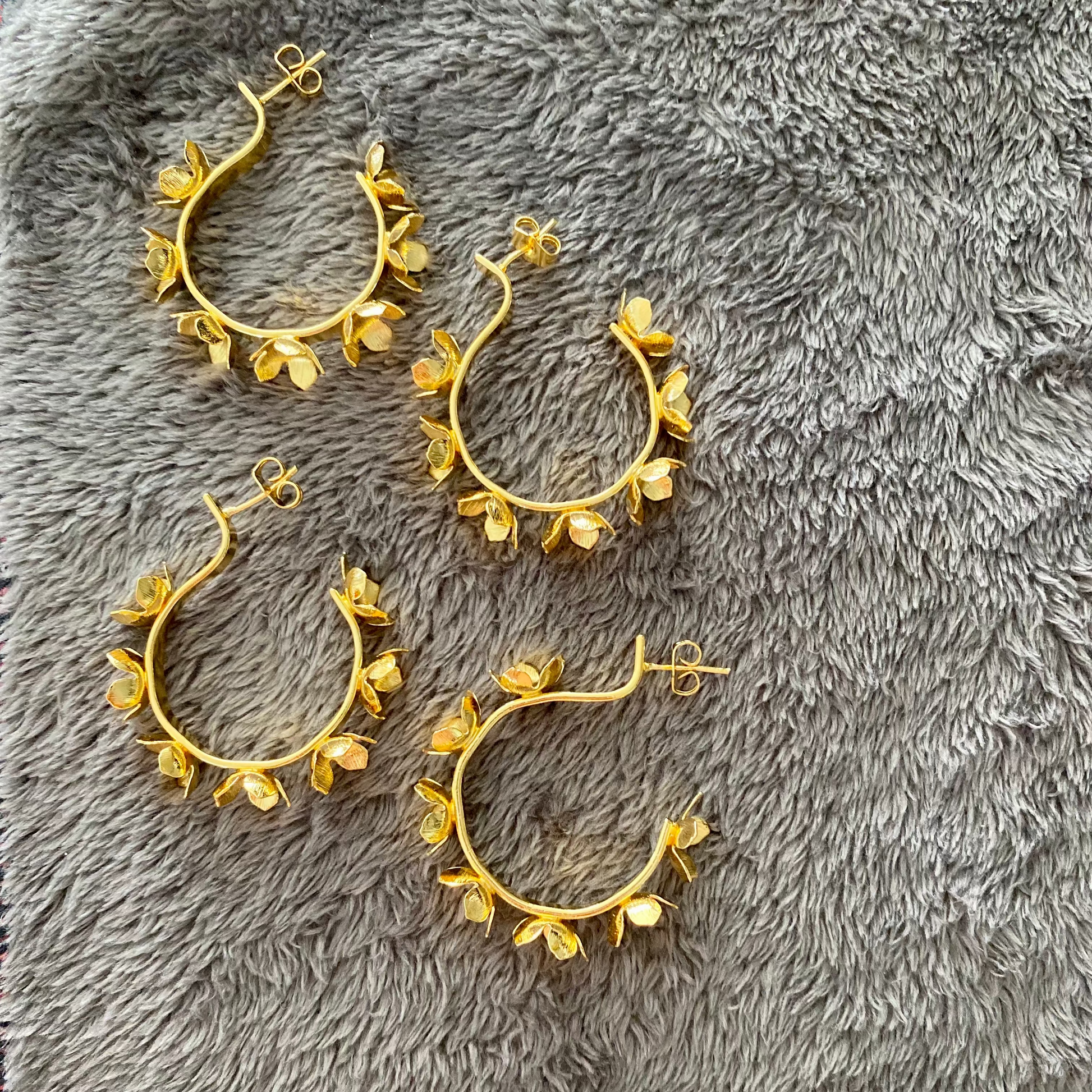 Gold hoop earrings with floral designs on a gray textured surface