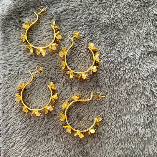 Gold hoop earrings with floral designs on a gray textured surface