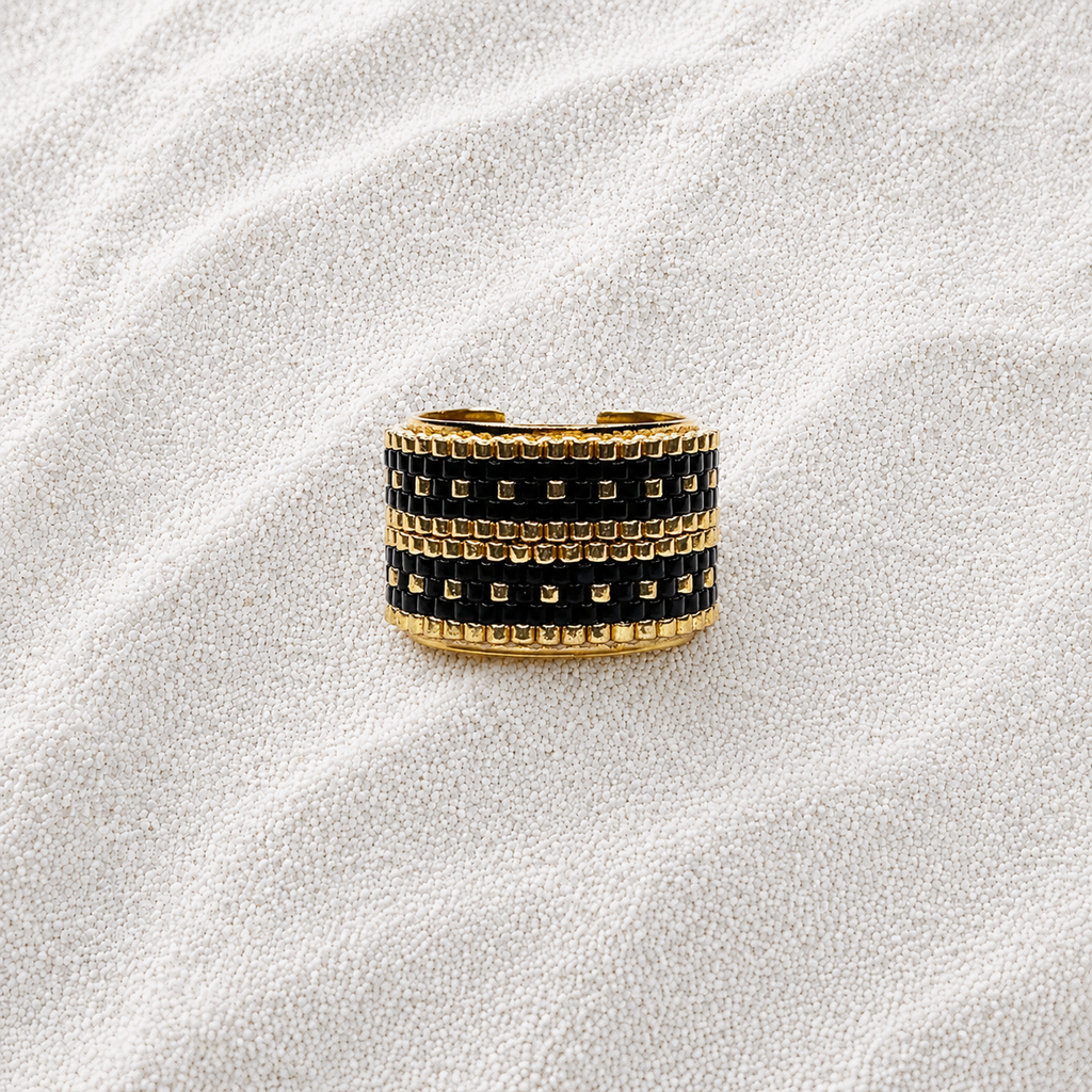A wide gold-tone ring with three rows of black square stones, photographed on a textured white fabric background.