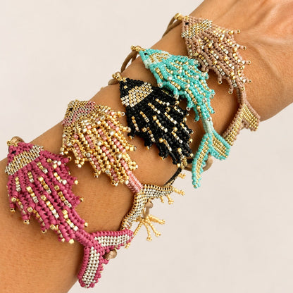 Four beaded bracelet-style wristbands with starfish motifs in pink, black, turquoise, and gold, shown worn on a person's wrist against a plain light background.