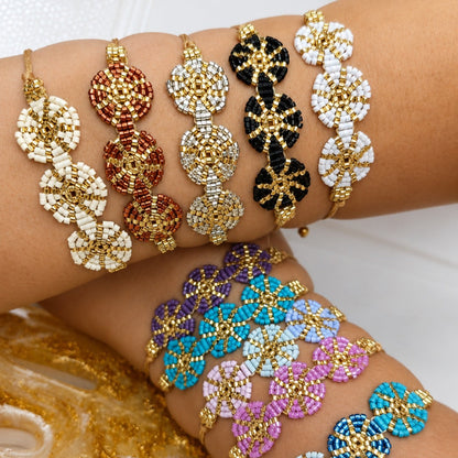 A set of beaded stretch bracelets displayed on a person's wrist and forearm. The bracelets feature gold-tone metal settings with multi-colored seed beads in white, red, black, blue, purple, pink, and light blue.