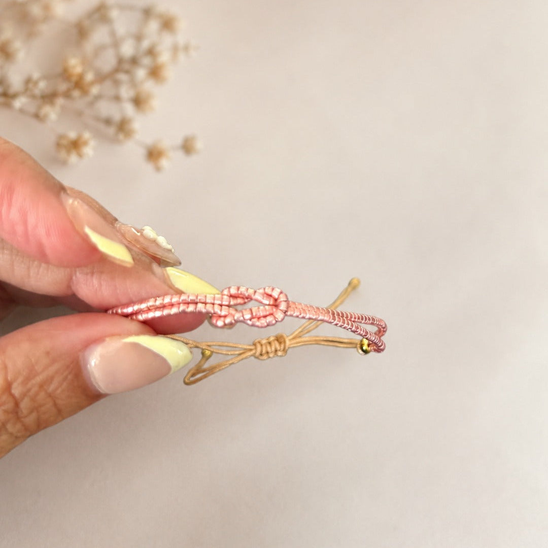 A close-up of a hand holding a delicate pink and gold beaded hair claw clip against a soft beige background with blurred dried flowers.