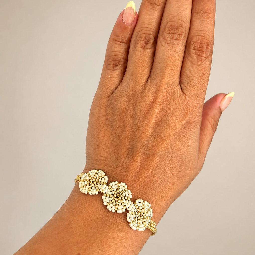 A close-up of a hand and wrist wearing a delicate gold bracelet adorned with three round, textured floral clusters.