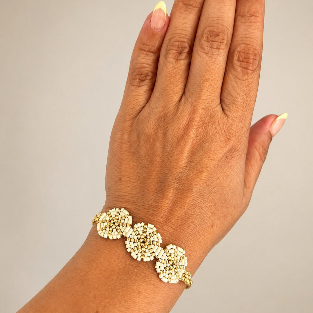 A close-up of a hand and wrist wearing a delicate gold bracelet adorned with three round, textured floral clusters.