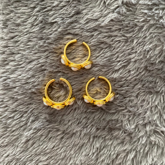 Three gold ear cuff with pearl-like stones on a gray fluffy surface