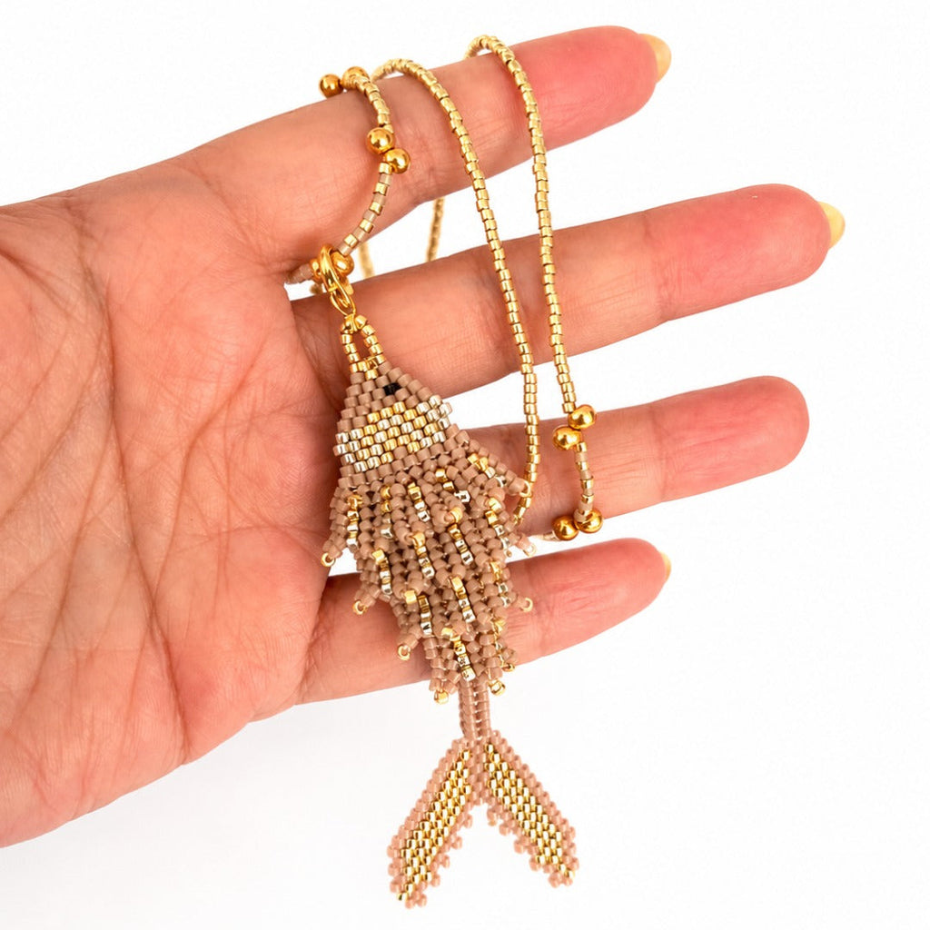 A gold beaded fish pendant necklace with a matching beaded chain, held in a person's hand against a white background.