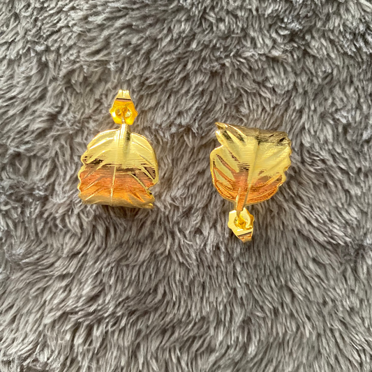 Gold leaf-shaped earrings on a gray textured surface