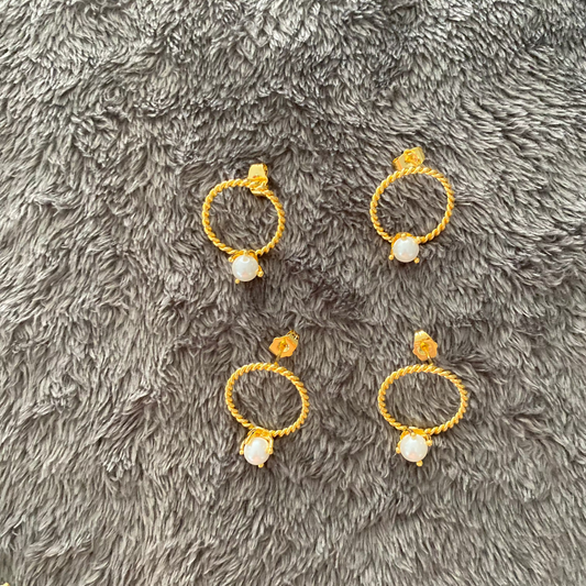 Gold hoop earrings with pearls on a gray textured surface