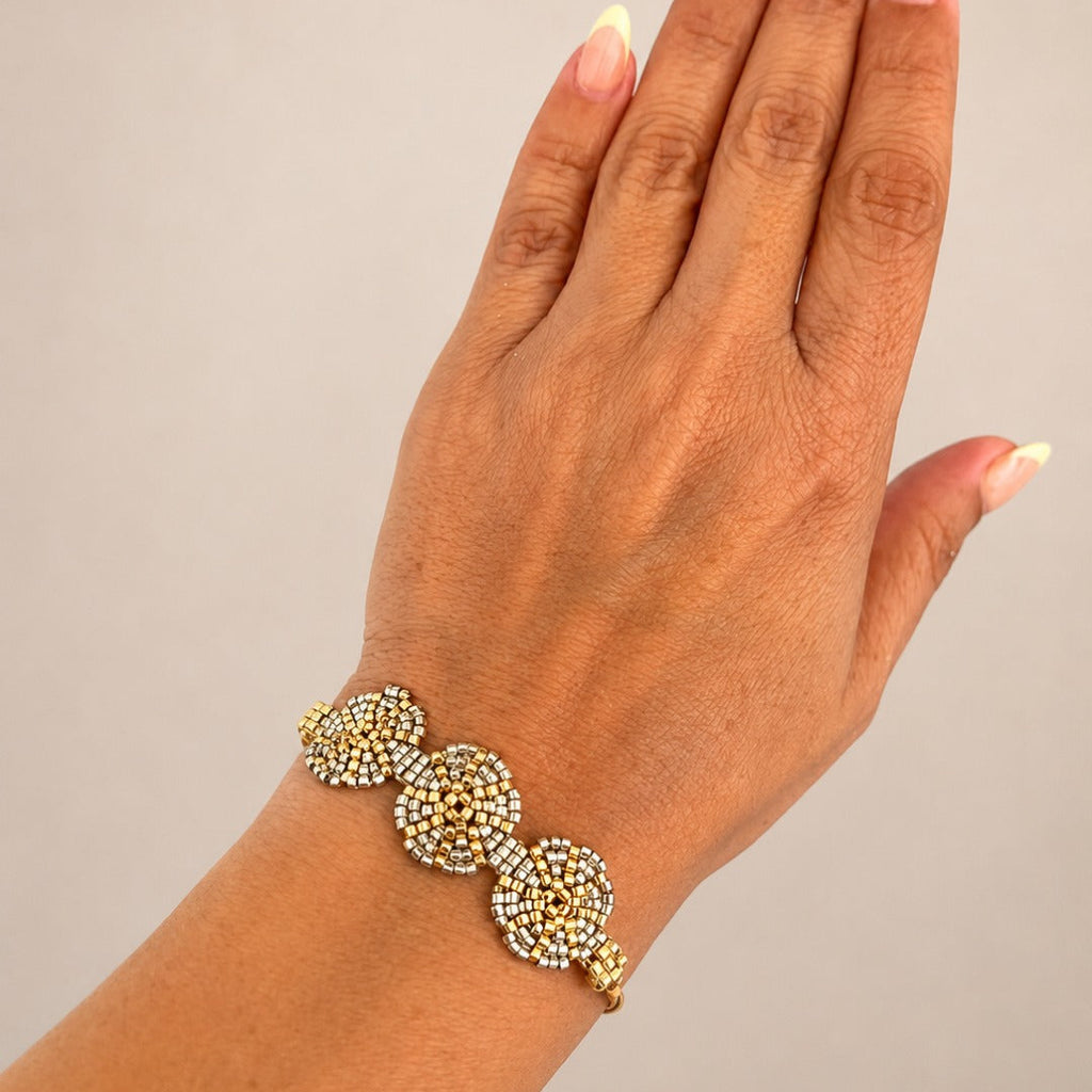 A gold-toned beaded bracelet with three circular floral clusters worn on a person's wrist, shown against a plain light gray background.