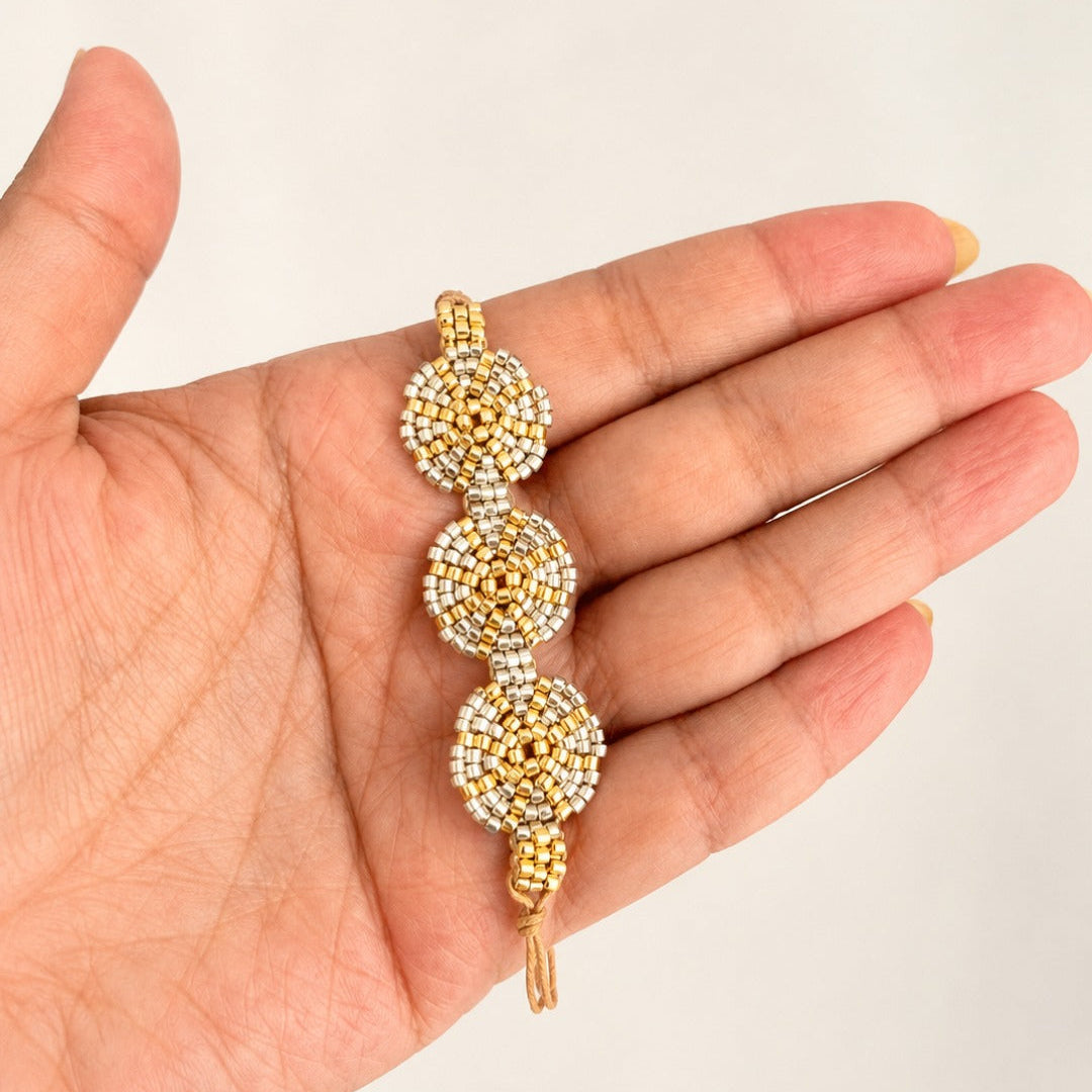 A gold and white beaded bracelet with three circular motifs, held in a person's hand against a plain light background.
