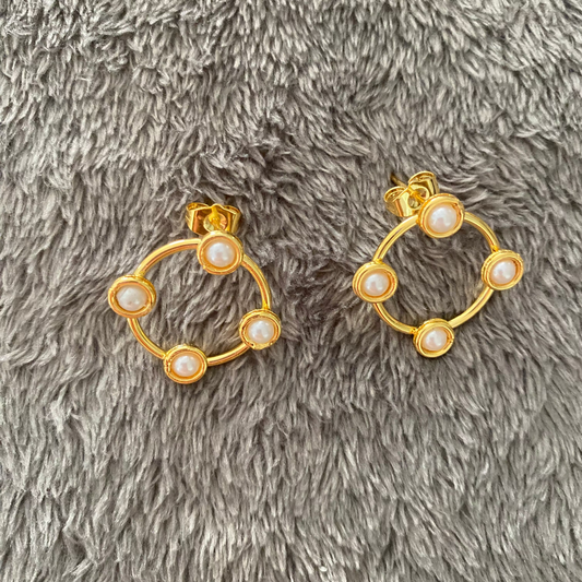 Gold hoop earrings with pearl-like stones on a gray textured surface
