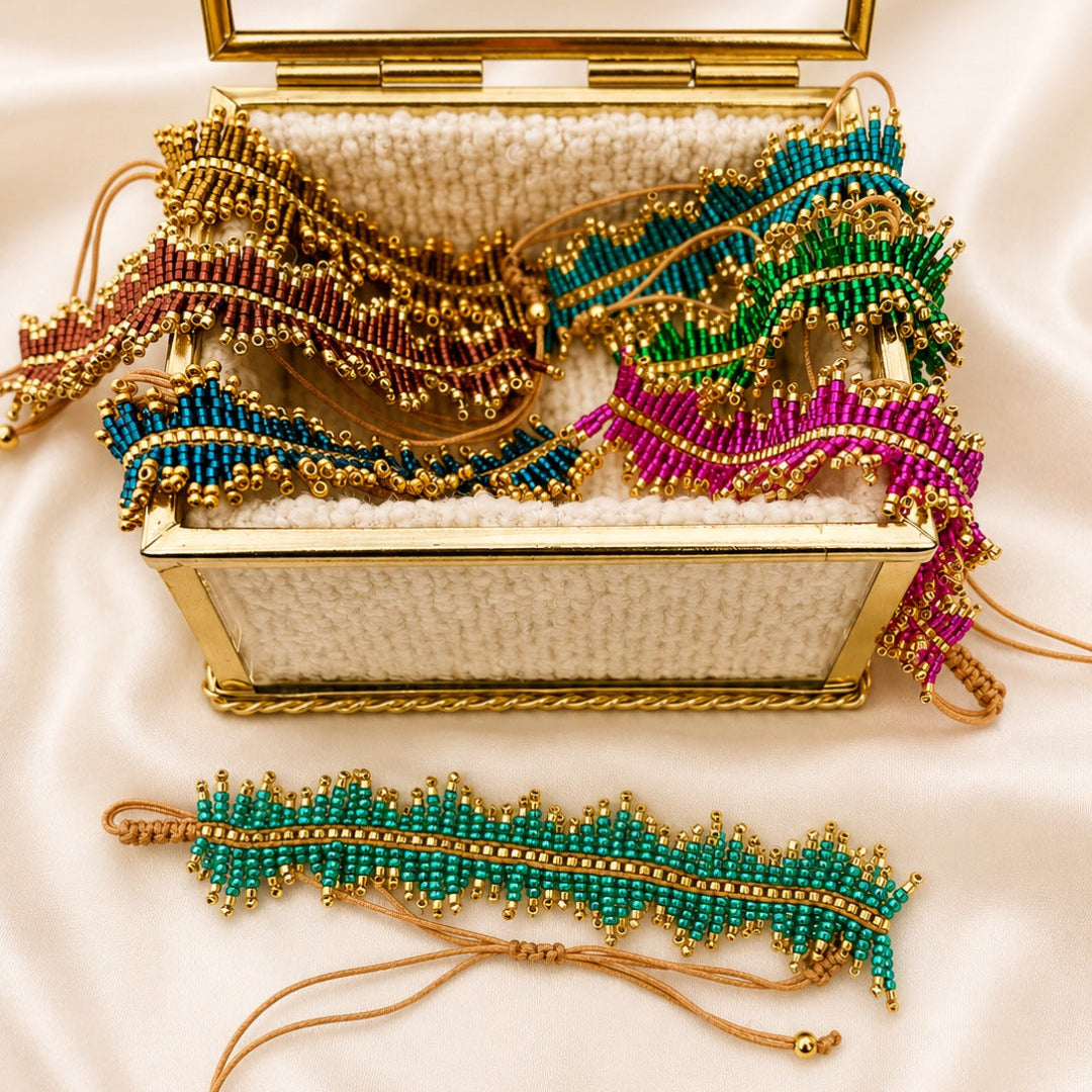 A gold-framed clutch bag with a white beaded interior is open on a cream satin background, displaying several matching beaded wristlet and anklet-style accessories in green, blue, pink, and purple with gold trim.
