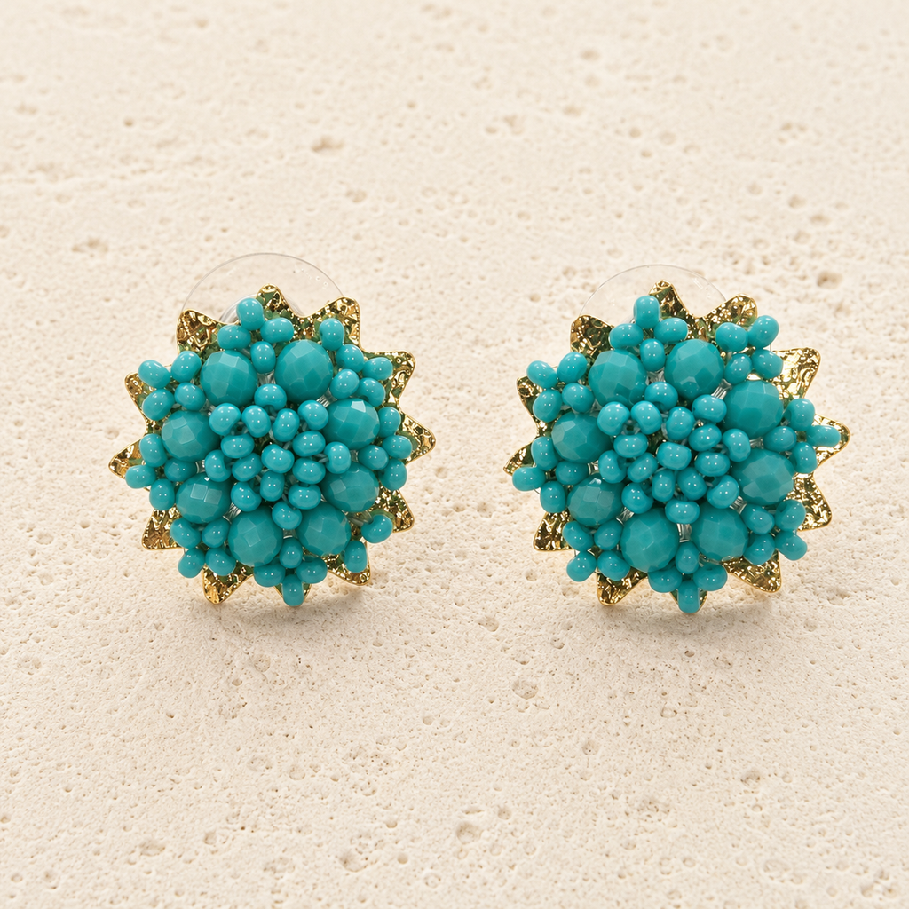A pair of gold and turquoise floral stud earrings displayed on a textured beige surface.