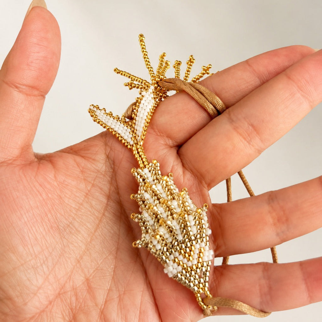 A gold and white beaded shell-shaped pendant or brooch held in a person's hand against a plain light background.