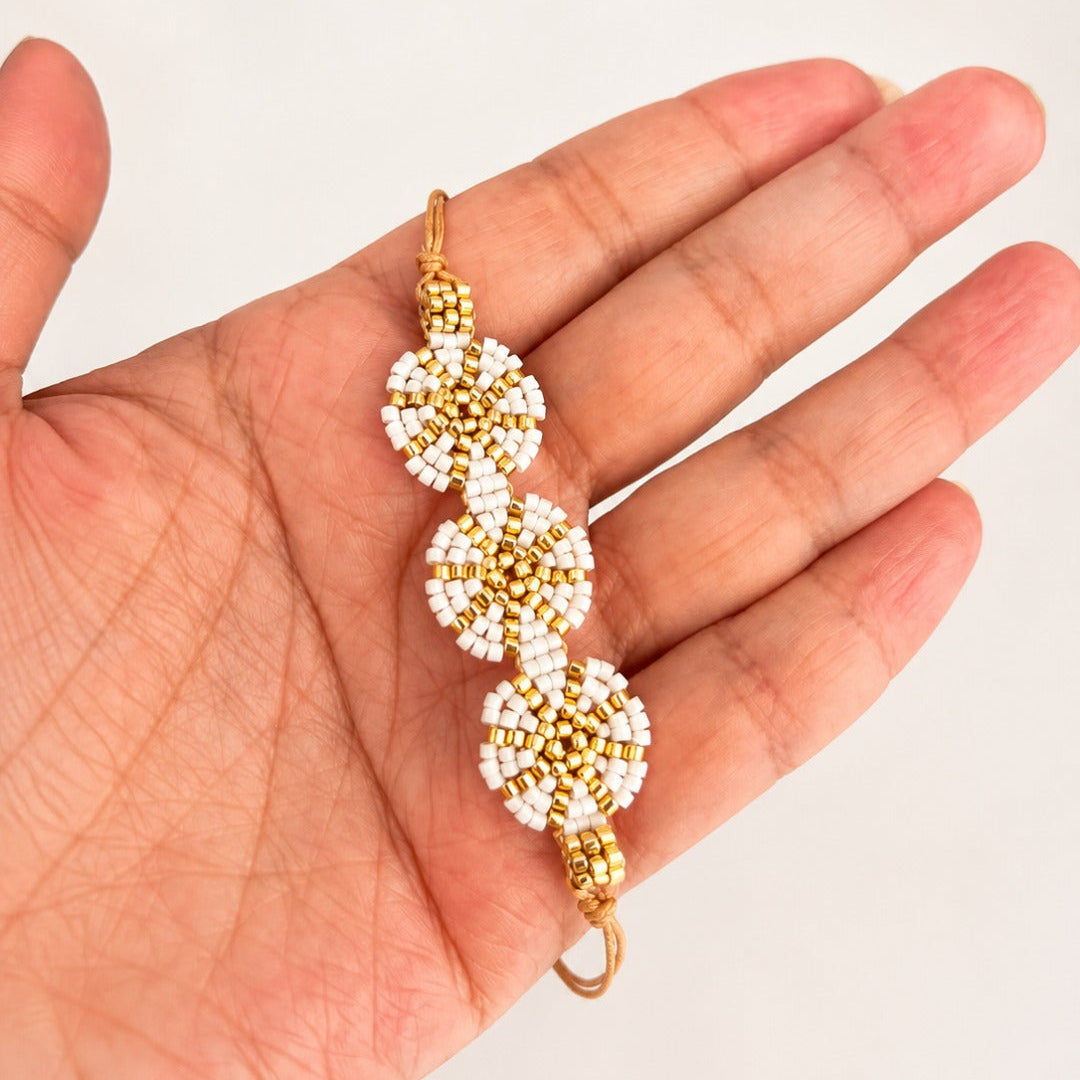 A handmade beaded bracelet with three gold and white flower-like clusters, held in a person's hand against a plain light background.