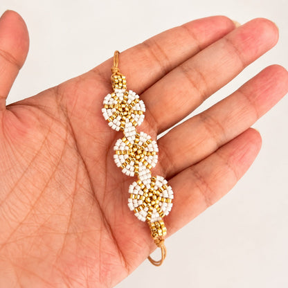 A handmade beaded bracelet with three gold and white flower-like clusters, held in a person's hand against a plain light background.