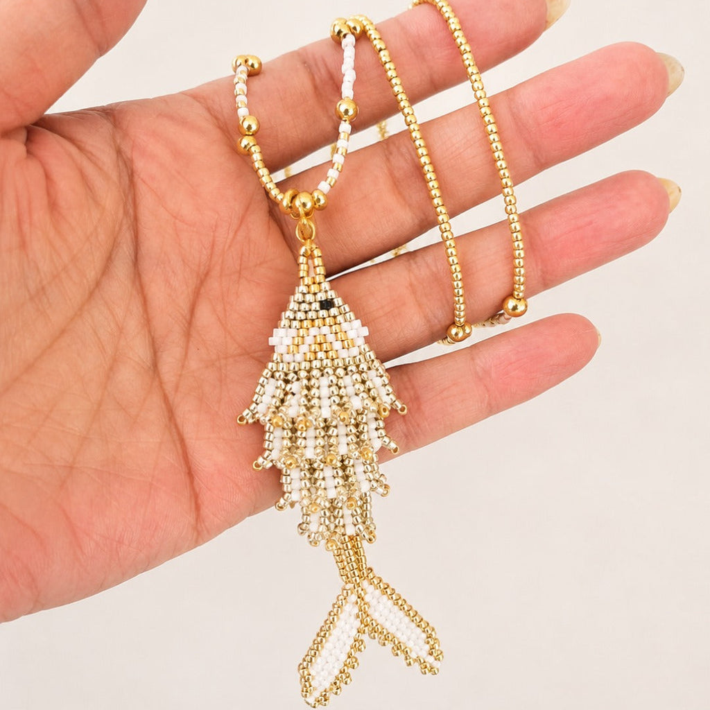A gold beaded necklace with a large, tiered tassel pendant held in a person's hand against a plain light background.